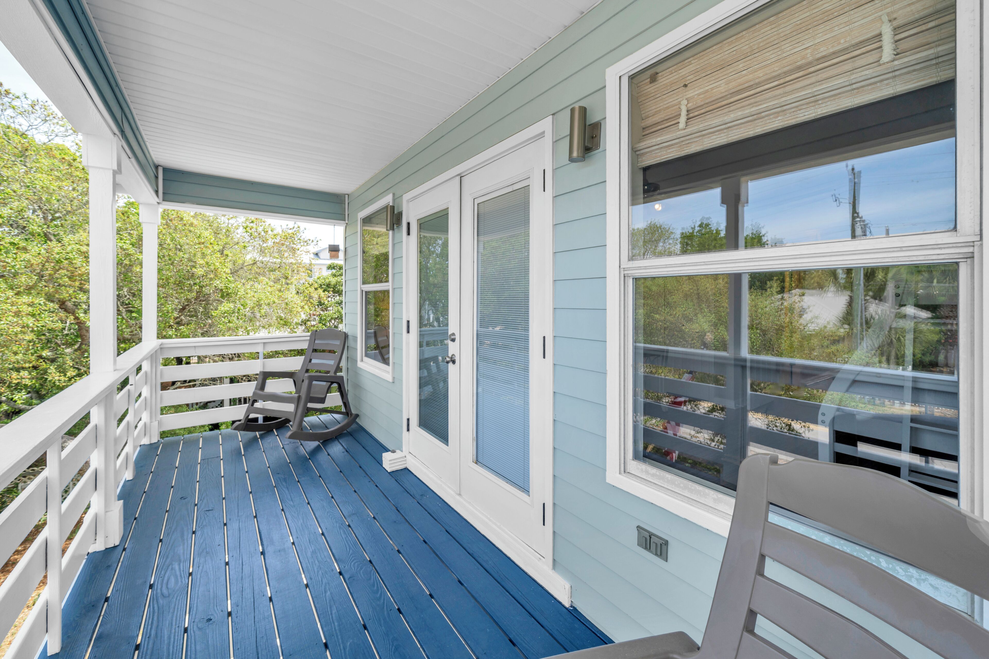 A covered porch with a blue floor, white railings, and two rocking chairs.
