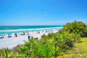 Ein Strand mit weißem Sand, klarem, blauem Wasser und grüner Vegetation.