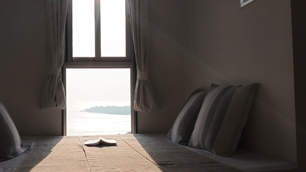 Een kamer met een bed, een raam met gordijnen en uitzicht op zee.