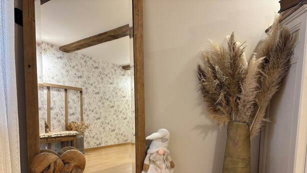 Habitació amb terra de fusta, un mirall, una escultura de fusta amb forma de cor, un animal de peluix i flors de ploma en un vas.