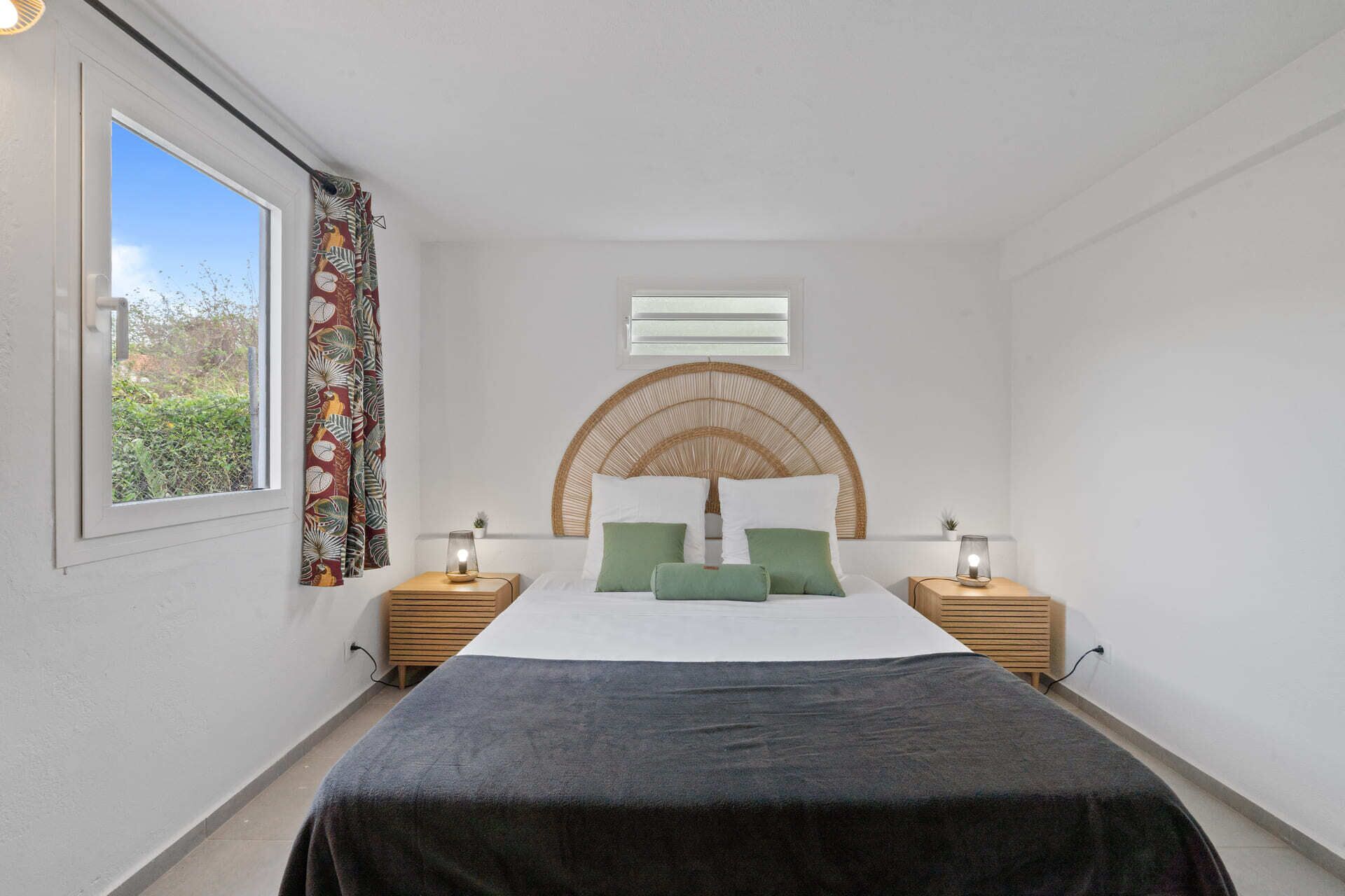 Een slaapkamer met een bed, twee nachtkastjes, een raam en uitzicht op groen.