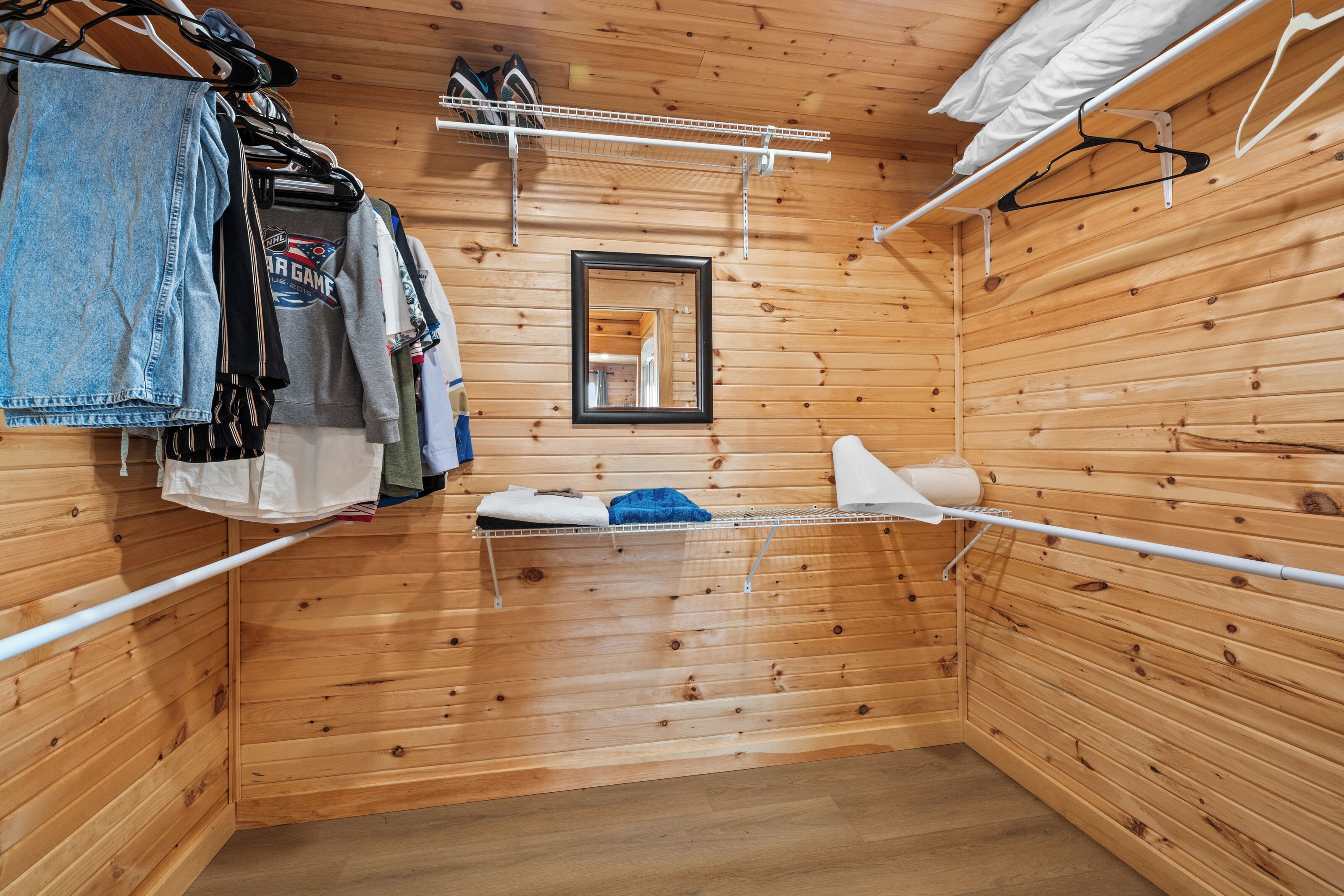 A wooden cabin interior with a hanging clothes rack, a mirror, and a small shelf with items.