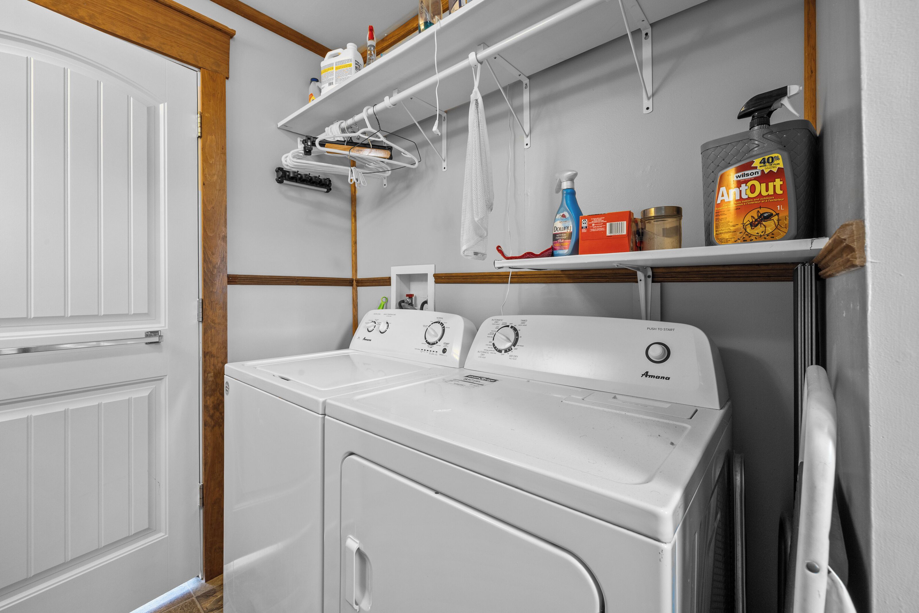 Un espace buanderie comprenant un lave-linge et un sèche-linge à chargement frontal, une étagère avec des produits de nettoyage et une porte avec un cadre en bois.