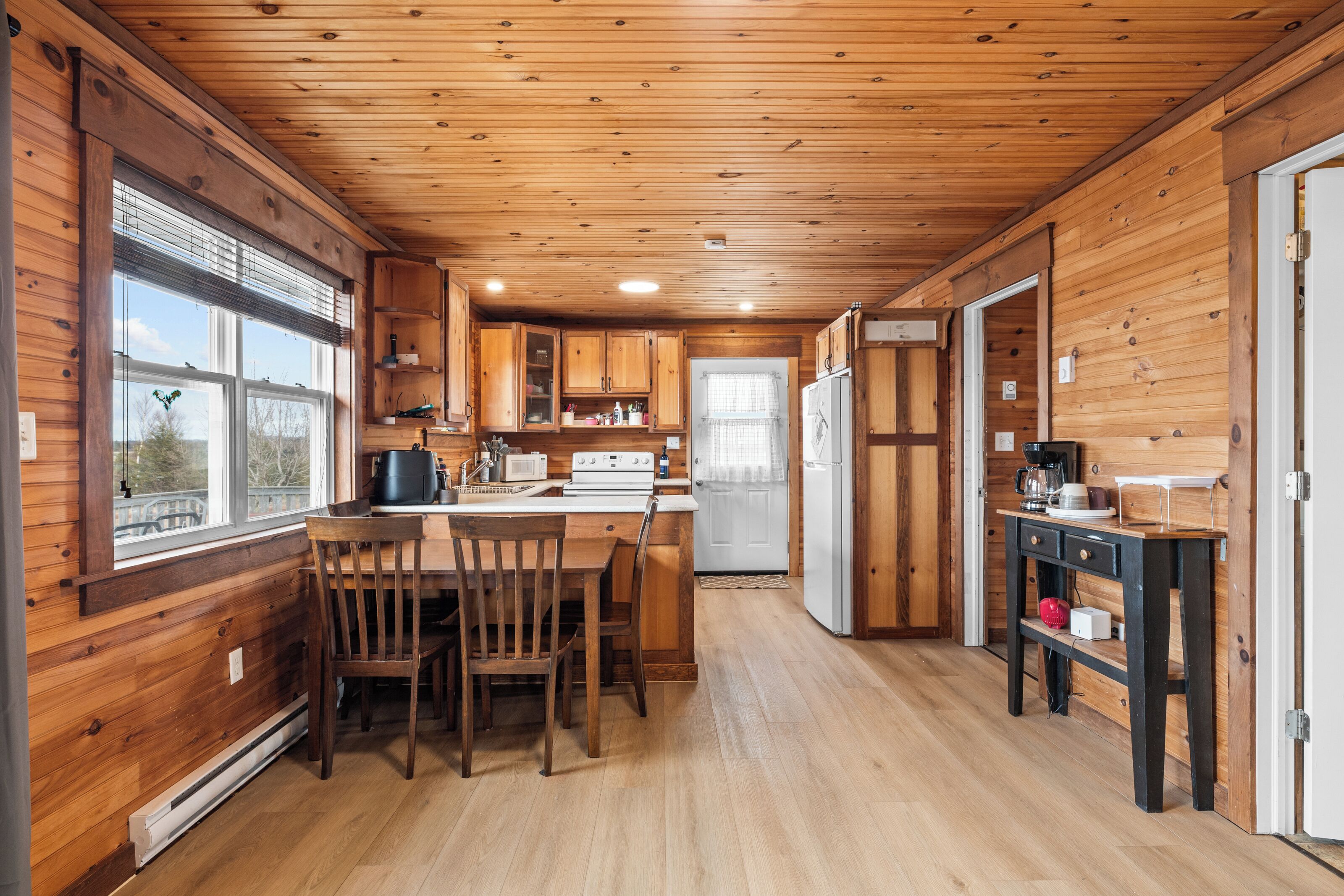 A wooden cabin interior with a kitchen, dining area, and a refrigerator.
