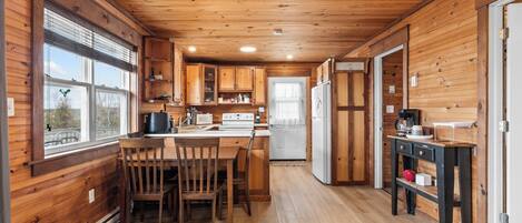 A wooden cabin interior with a kitchen, dining area, and a refrigerator.