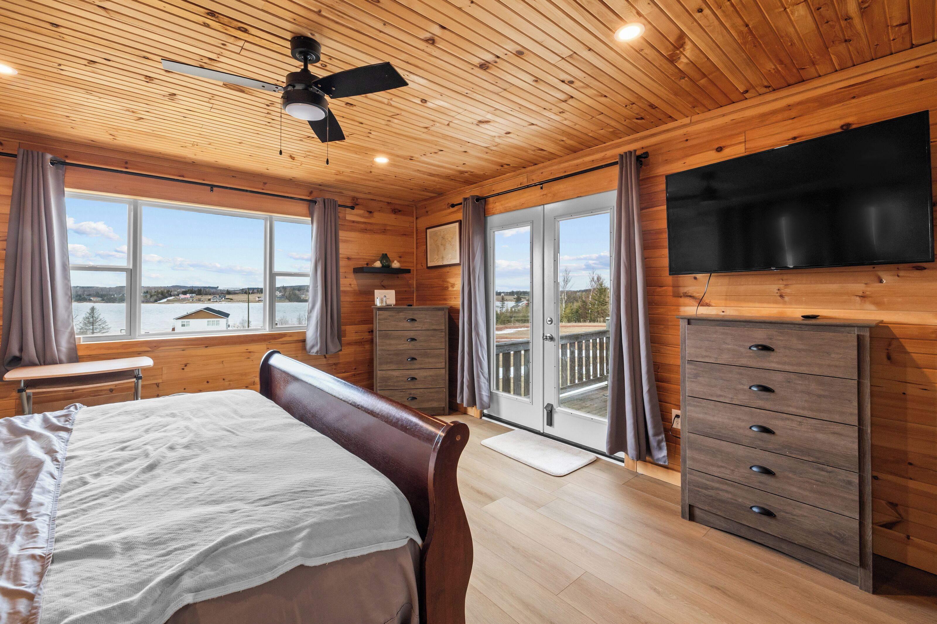 A bedroom with a bed, a dresser, a television, and a balcony with a view.