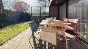 Eine Terrasse im Freien mit Tisch und Stühlen, eine Glastür und eine Rasenfläche.