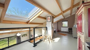 Ein Zimmer mit Oberlichtern, einer Holzbalkendecke, einem weißen Boden, einer roten Tür und einem kleinen Holzstuhl.