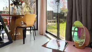Ein modernes Zimmer mit einem großen Fenster, einem Holztisch, einem gelben Stuhl und einer Zeitschrift auf einem kleinen Tisch.