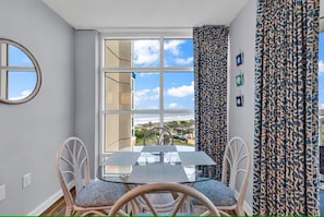 A room with a glass table and chairs, a large window with a view, patterned curtains, and a round mirror on the wall. - Fabulous 2-bedroom condo with AC in Myrtle Beach (Myrtle Beach)
