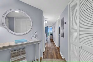 A hallway with a mirror, a sign reading 'BEACH RULES soak up the sun,' and a view into another room. - Fabulous 2-bedroom condo with AC in Myrtle Beach (Myrtle Beach)