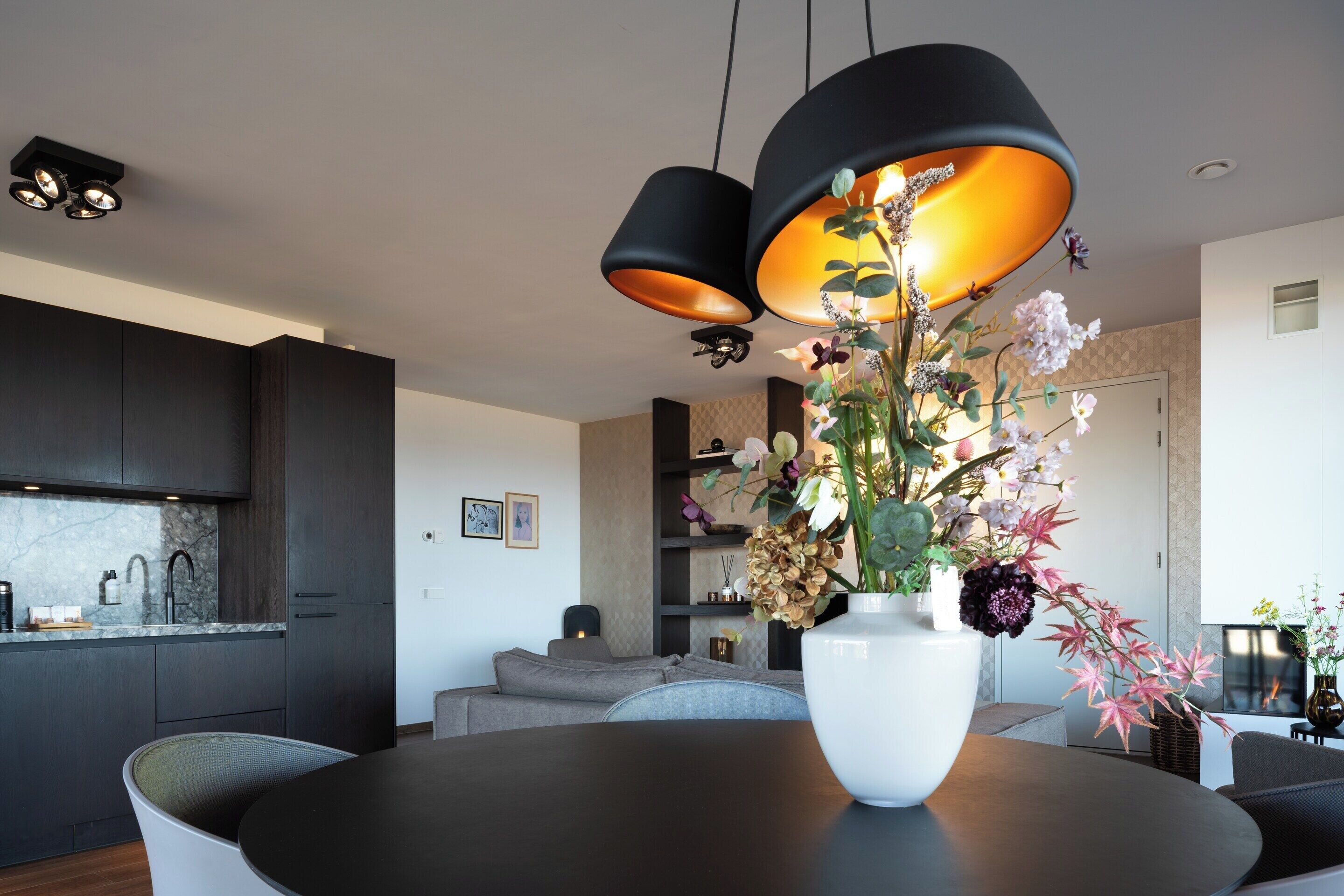 A modern kitchen with dark cabinetry, a marble countertop, and a dining area with a round table and chairs.