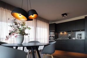 A modern kitchen with dark cabinetry, a built-in oven, and a countertop with a coffee machine. - Luxury Seaview Apartment for 4 (Egmond aan Zee)