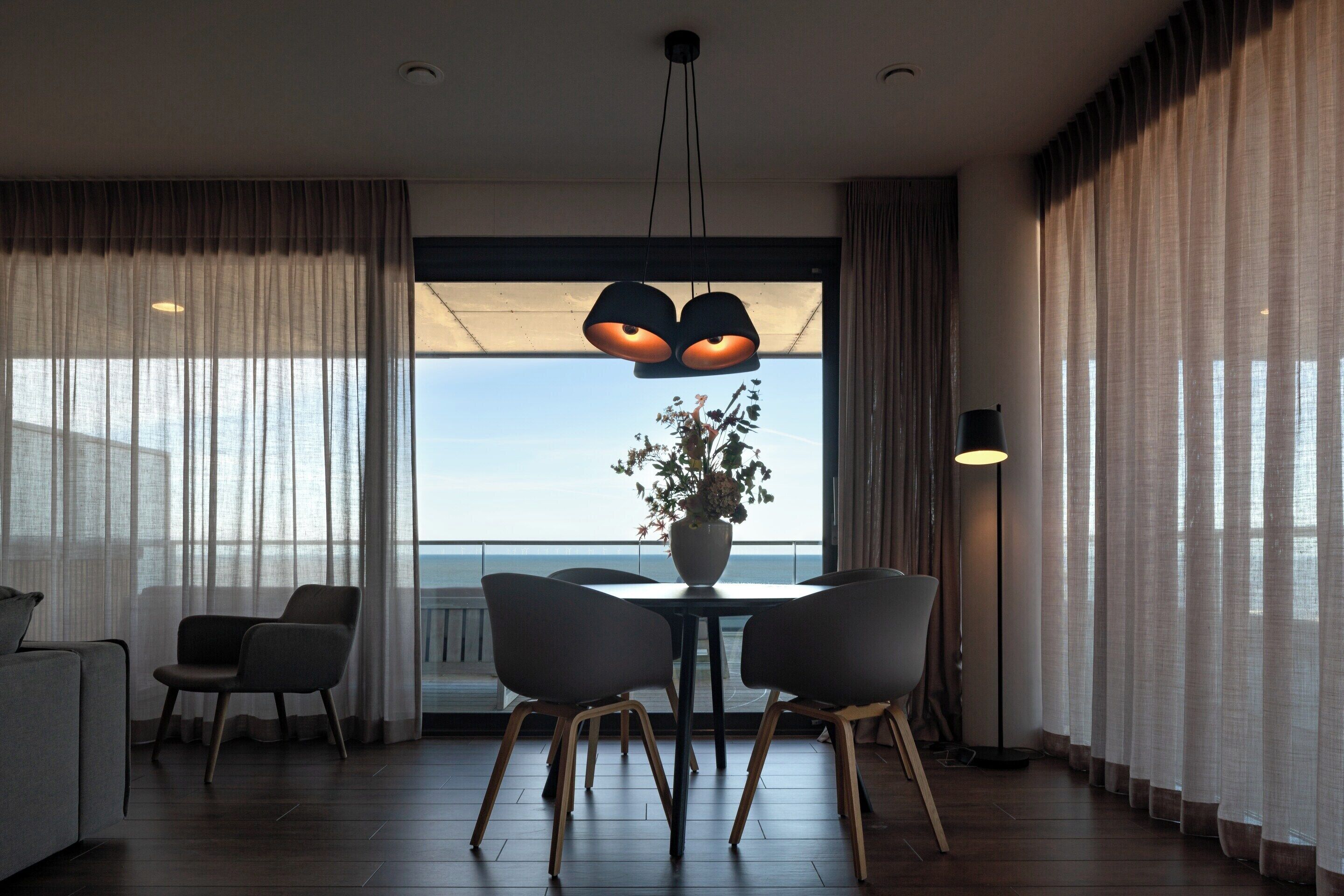 Ein moderner Essbereich mit Tisch, Stühlen, einer Blumenvase und Meerblick.