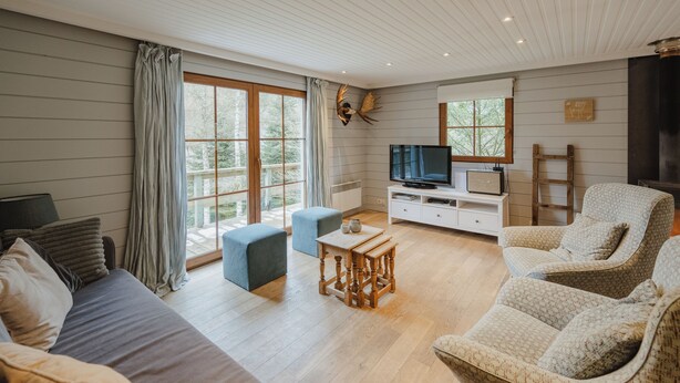 Ein modernes Wohnzimmer mit einer Couch, zwei Sesseln, einem Fernseher und einem Holztisch.