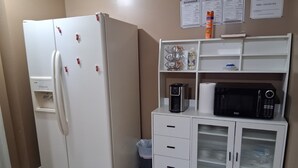 A kitchenette with a white refrigerator, coffee maker, microwave, and a small cabinet with drawers.