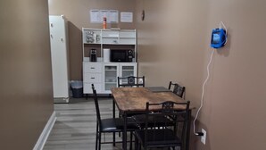 A dining area with a wooden table and chairs, a white refrigerator, a microwave, and a coffee maker on a white cabinet.