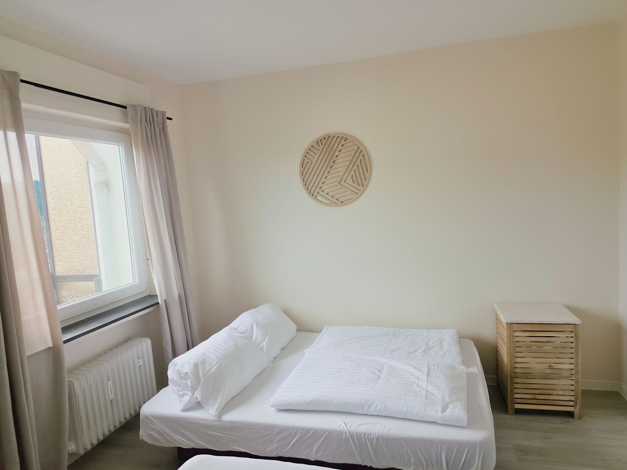 Ein Schlafzimmer mit Bett, Heizkörper, einem fenster mit Vorhängen und einem Wanddekor.