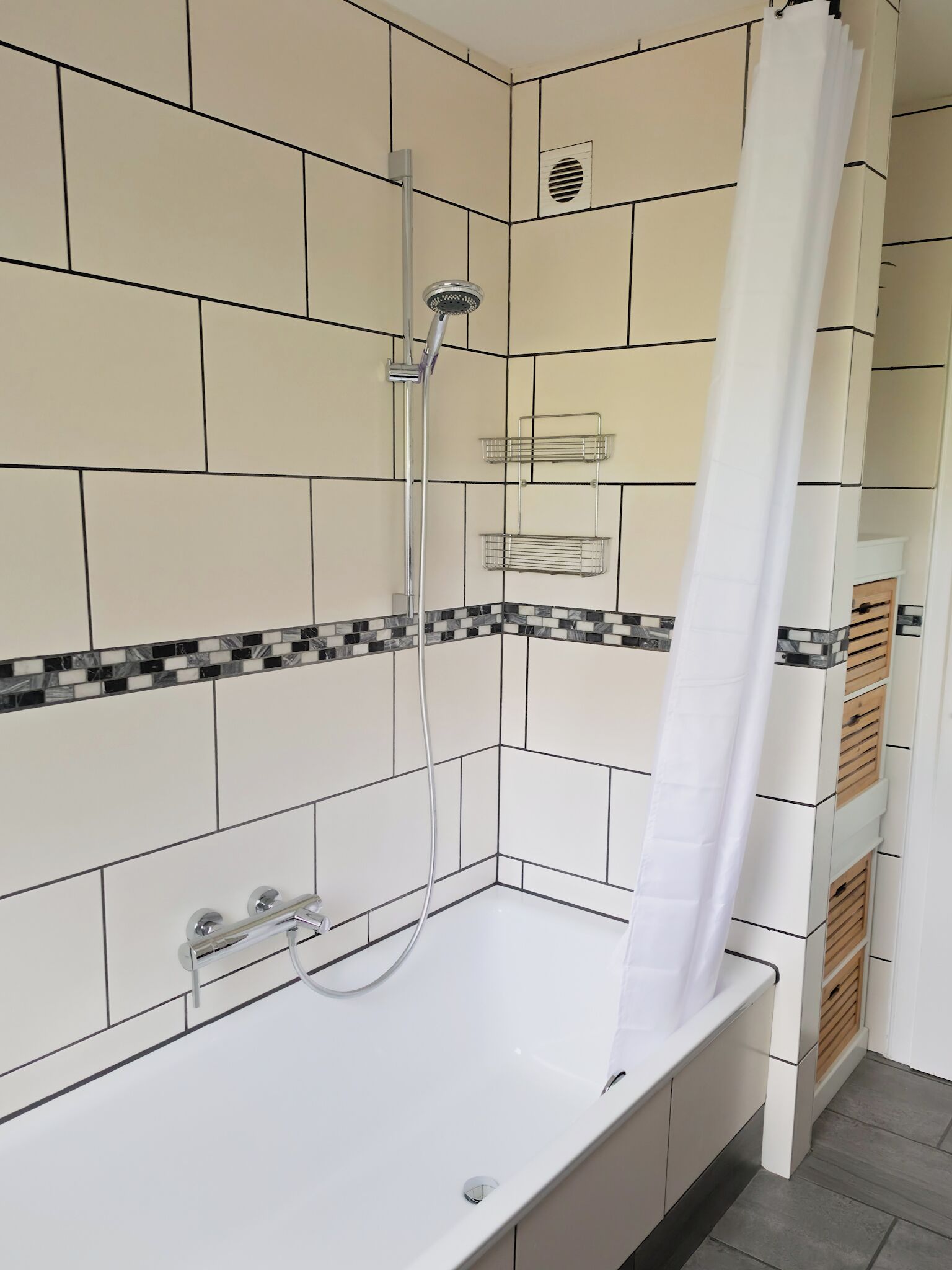 A bathroom with a white bathtub, a shower, and a tiled wall with a black and white border.