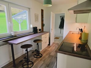 Una cocina con ventana, un lavamanos, taburetes y una puerta que da a otra habitación.
