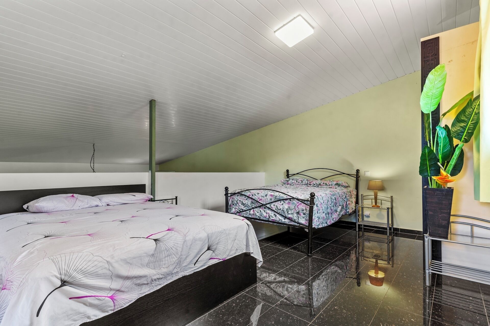 A bedroom with two beds, a ceiling light, a plant, and a metal shelf.