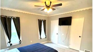 A bedroom with a bed, a ceiling fan, a window with curtains, a door, and a wall-mounted TV. - (H2) 2 Bdrm Apt Inner Harbor (Syracuse)