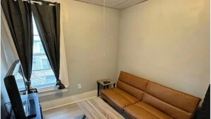 A room with a sofa, a small table, a TV, and a window with curtains. - (H2) 2 Bdrm Apt Inner Harbor (Syracuse)