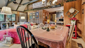 Interior acogedor de una cabaña con una mesa de comedor, sillas, una araña y una zona de cocina.