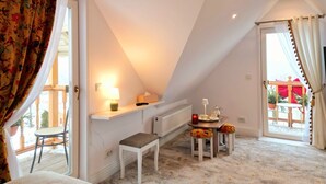 A cozy attic bedroom with a sloped ceiling, a small table with a lamp, a bench, and a view of the outside balcony.