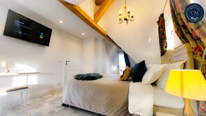 A bedroom with a bed, a TV mounted on the wall, a chandelier, and a window with curtains.