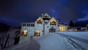 A large, multi-story building with balconies, illuminated windows, and a snowy landscape.
