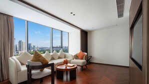 A modern living room with a sofa, armchair, and coffee table, large windows with a city view, and a flat-screen TV. - Howard Johnson By Wyndham Phnom Penh Tk (Phnom Penh)
