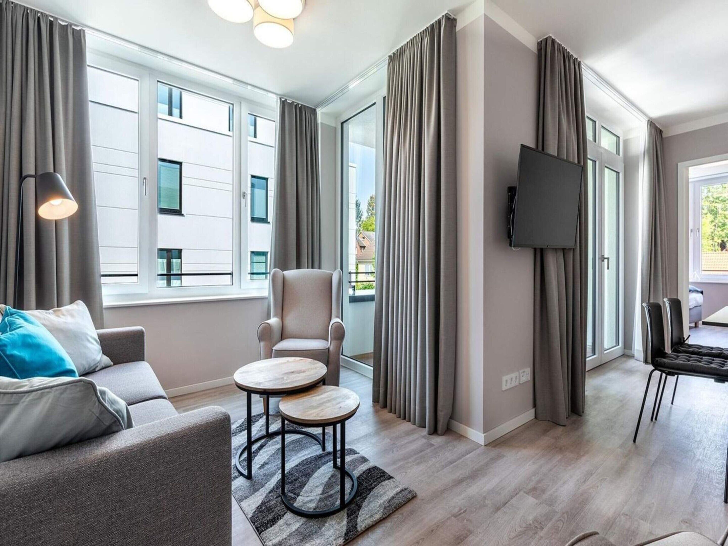 Un salon moderne comprenant un canapé, un fauteuil et une table basse, de grandes fenêtres, un téléviseur à écran plat et un coin repas.