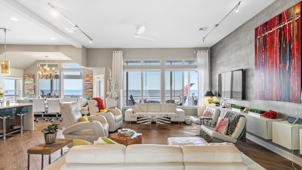 Un salón amplio con un sofá blanco grande, una zona de comedor con mesa blanca y una cocina con electrodomésticos modernos.