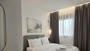 Siististi järjestetty hotellihuone, jossa on sänky, yöpöytä, lamppu ja ikkuna, jossa on verhot.