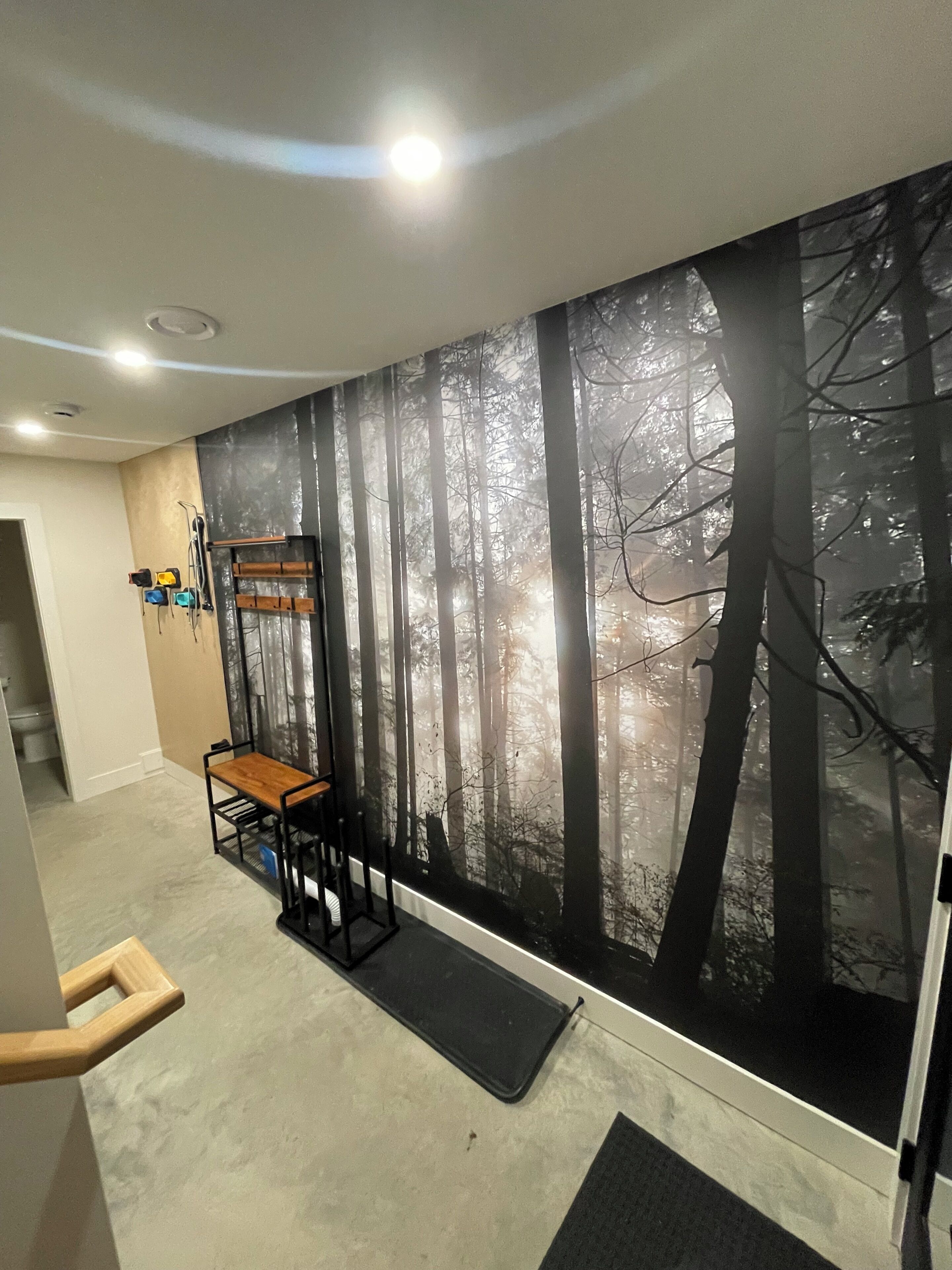 A room with a large wall mural of a forest, a wooden bench, a small table, and a door leading to another room.