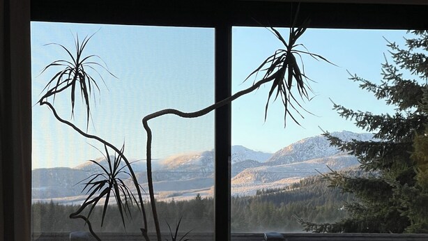 Un balcon avec une table, des chaises et une vue sur les montagnes et les arbres.