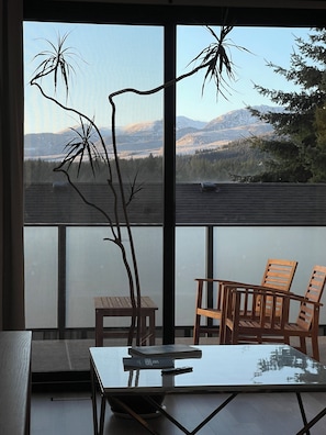 Un balcón con una mesa, sillas y vistas a montañas y árboles.