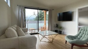 Un salon moderne comprenant un canapé, une table basse en verre, un fauteuil vert, un téléviseur à écran plat et une porte-fenêtre coulissante donnant sur un espace extérieur.