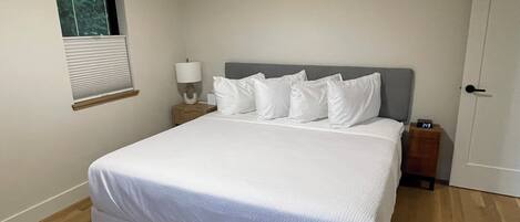 A bedroom with a bed, a nightstand, a lamp, a window, and a door.