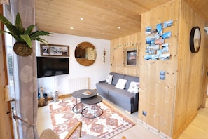 A cozy living room with a grey sofa, a round coffee table, and a wooden wall with a mirror and photos. - 2nd floor, balcony, ski locker, 45m², Les Gets (Les Gets)