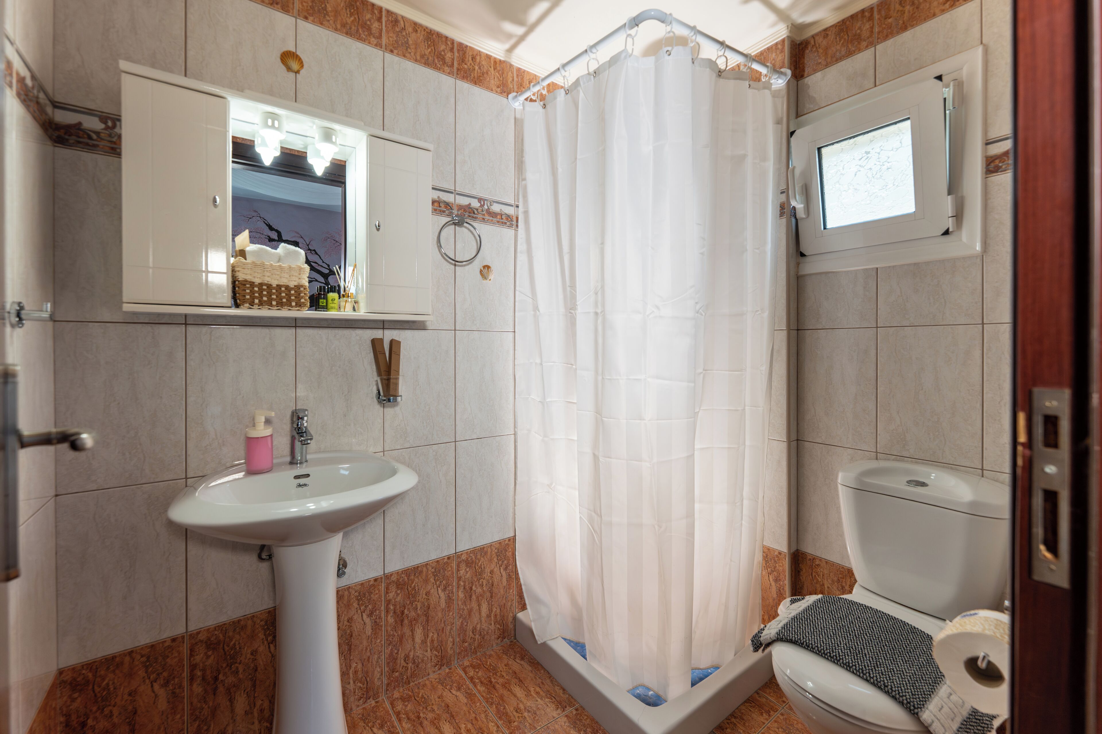 Un baño con lavamanos pedestal, inodoro, cortina de ducha y espejo sobre el lavamanos.