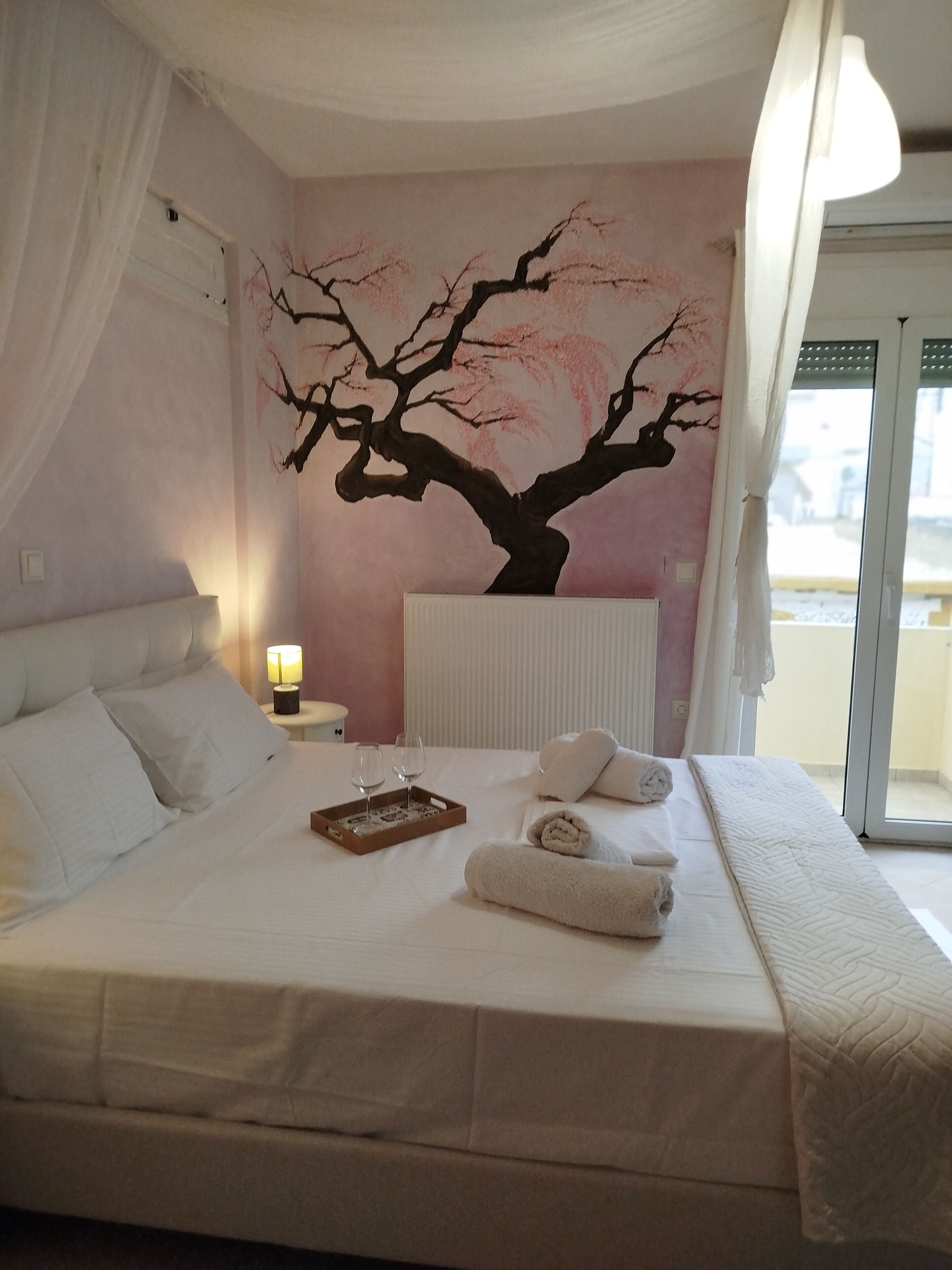 Une chambre à coucher avec un lit, des oreillers, une table de chevet avec une lampe, un plateau avec des verres et des serviettes.
