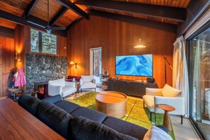 Ein modernes Wohnzimmer mit Kamin aus Stein, Holzboden und großem Fernsehbildschirm.