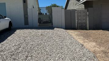 Uma entrada residencial com calçamento de cascalho, um carro branco estacionado à esquerda e um portão.