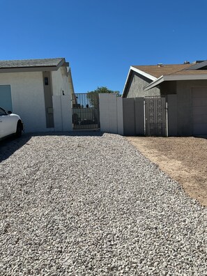 Uma entrada residencial com calçamento de cascalho, um carro branco estacionado à esquerda e um portão.