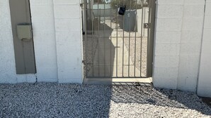 Ein begrenzter Eingangsbereich mit einem Metallgitter, einem Kiesweg und einem Gebäude mit weißen Wänden.