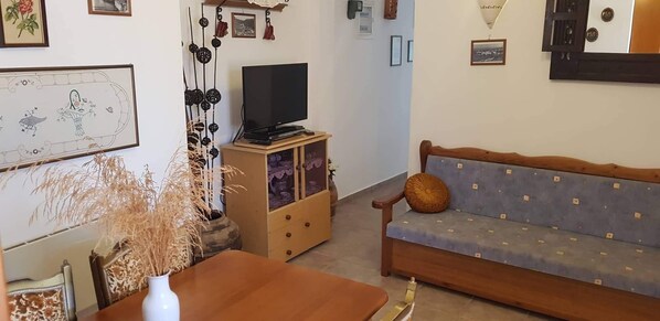 Ein Wohnzimmer mit einer Couch, einem Fernseher, einem Schrank und einem Wandbild.