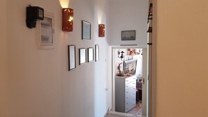 Een gang met ingelijste foto’s, wandlampen en een deur naar een kamer met een dressoir en decoratieve objecten.