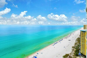 A beach with clear turquoise water, a sandy shore, and a tall building on the right. - ☀️Stunning Gulf Front | 2 Pools + Hot Tub | Ocean Villa 2306☀️ (Panama City Beach)